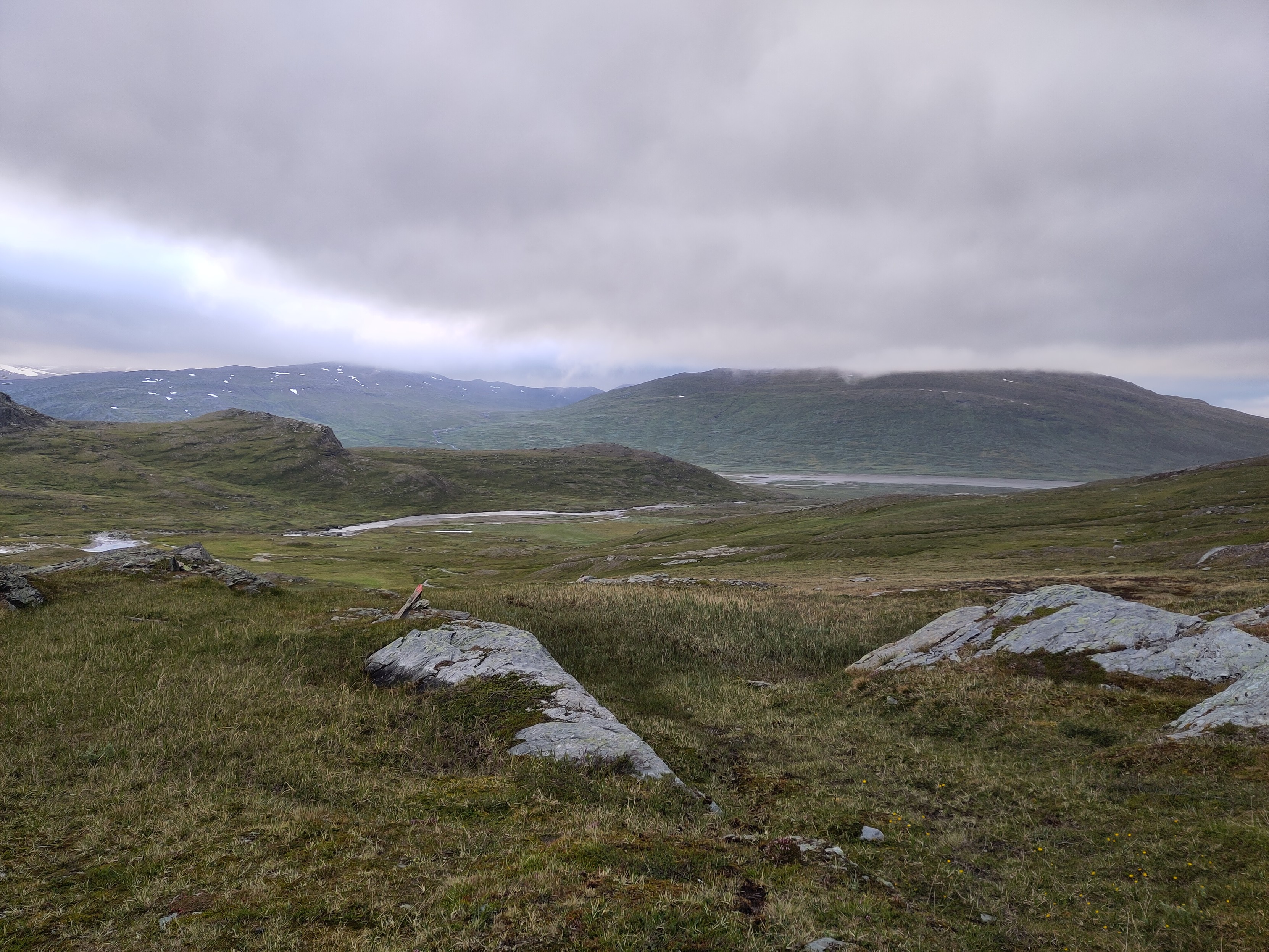 A view down from the mouth of the valley, where a meeting of two other valleys with streams meet far below. The clouds are starting to break up, but it is not very bright due to the lateness in the day.