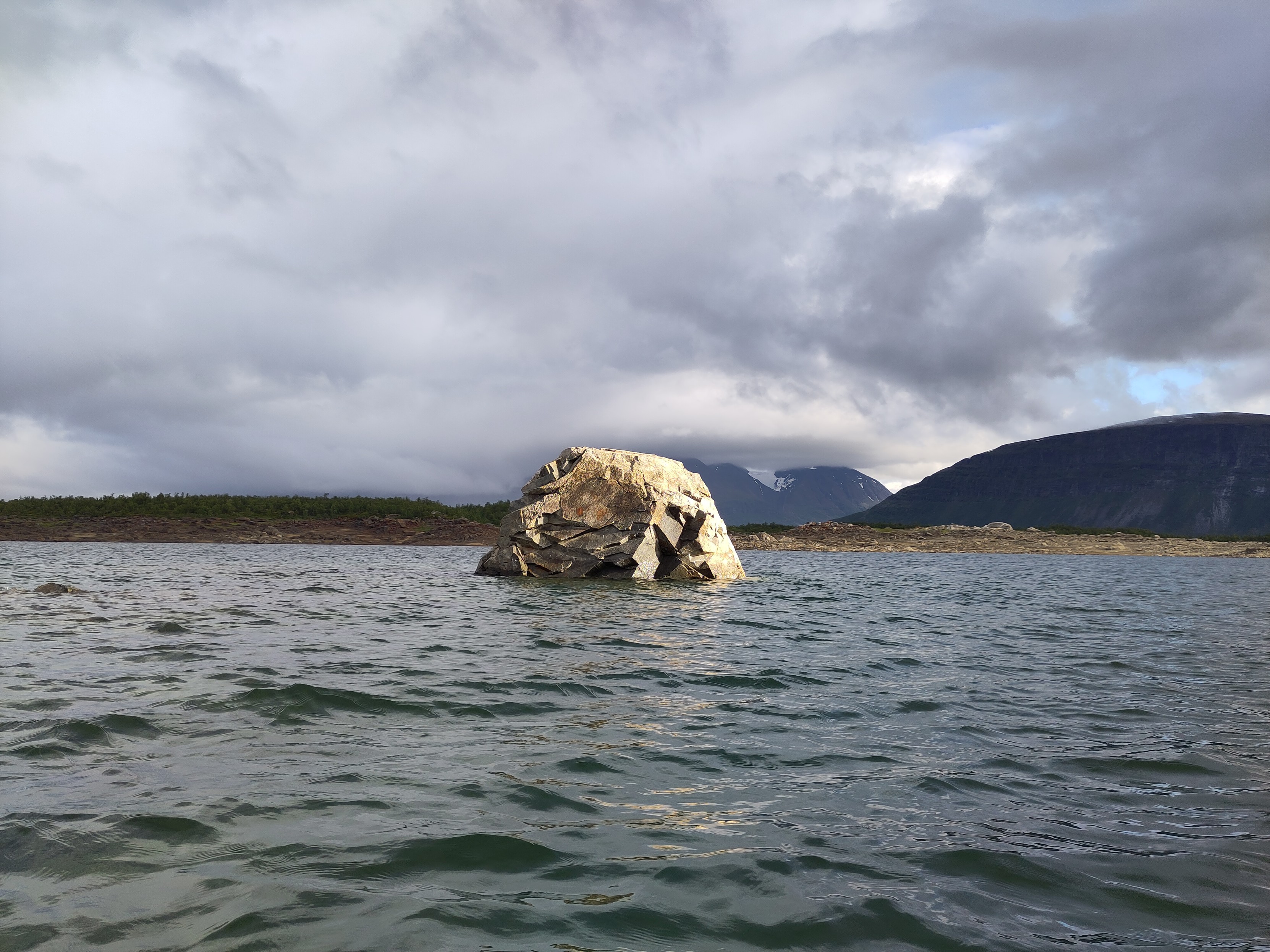 A singular angular rock breaking the surface of a lake.