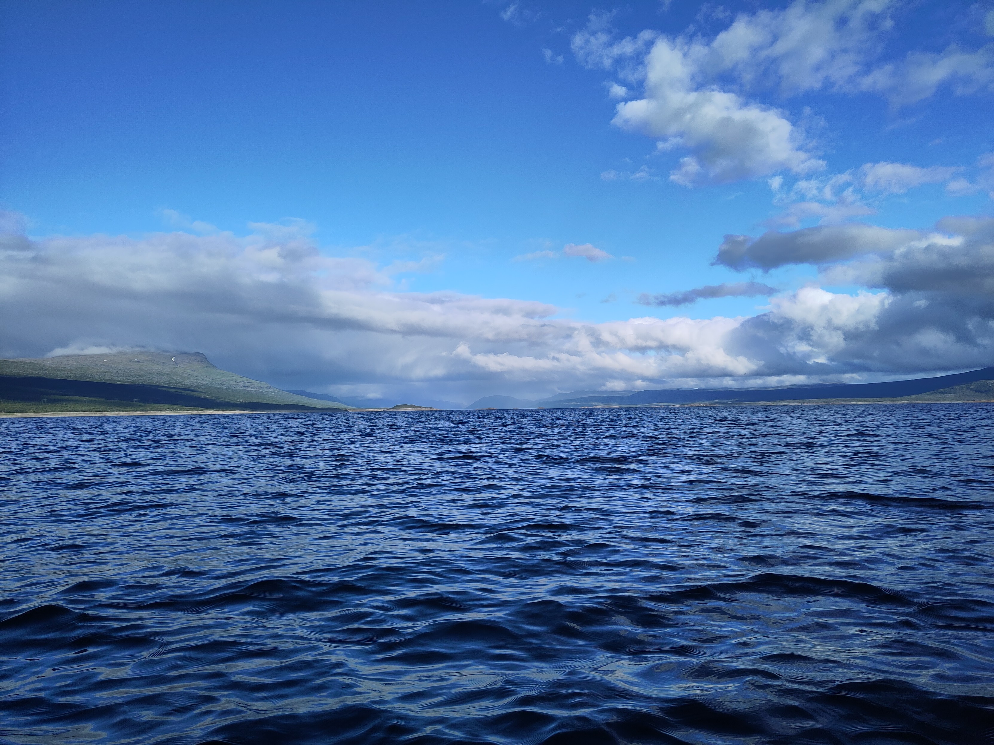 Blue water under blue sky leading away into infinity in the middle, on the sides shores can be seen far away.