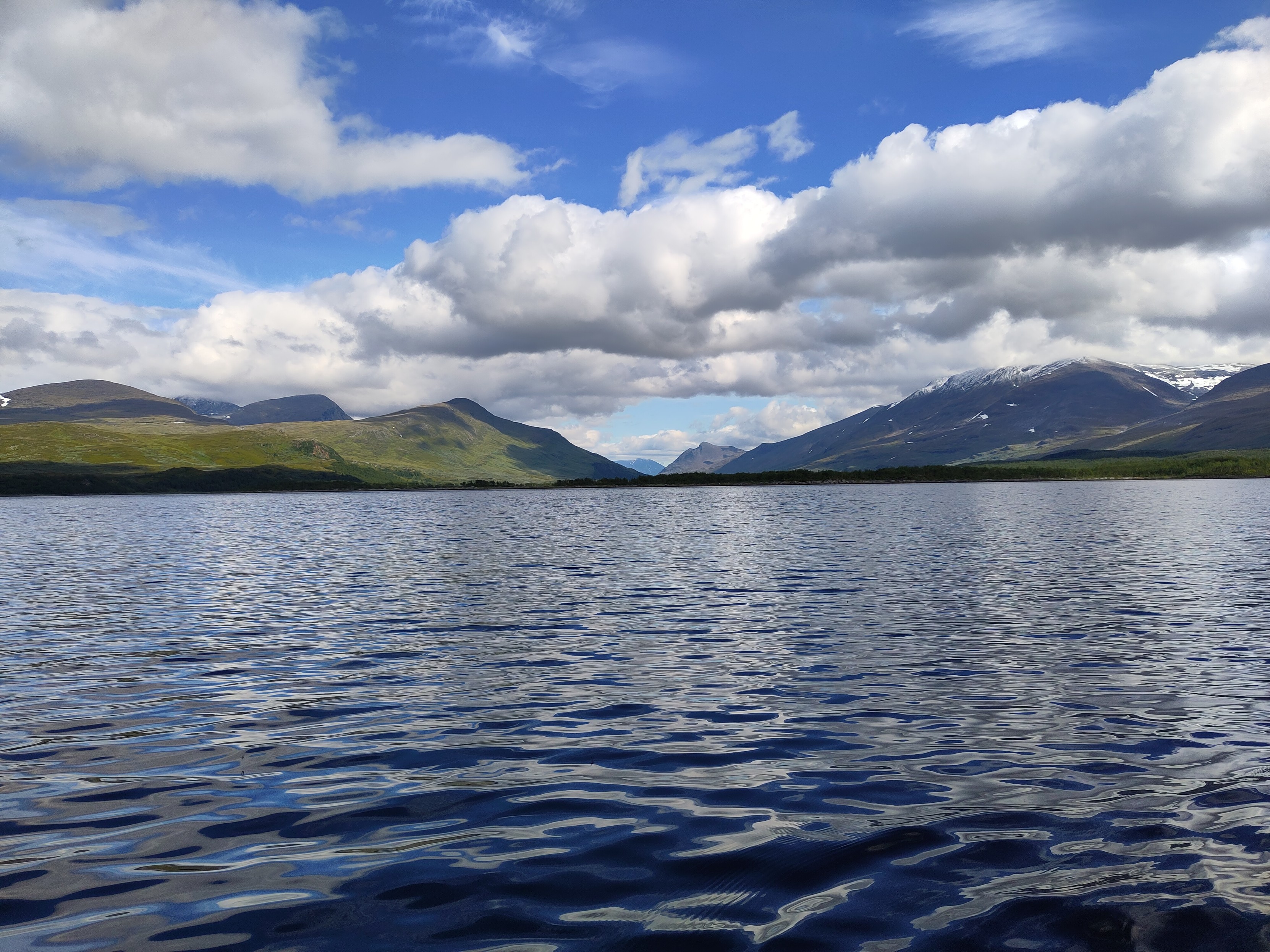 A view from a blue lake of a far mountain valley with fresh white snow on some if the peaks.