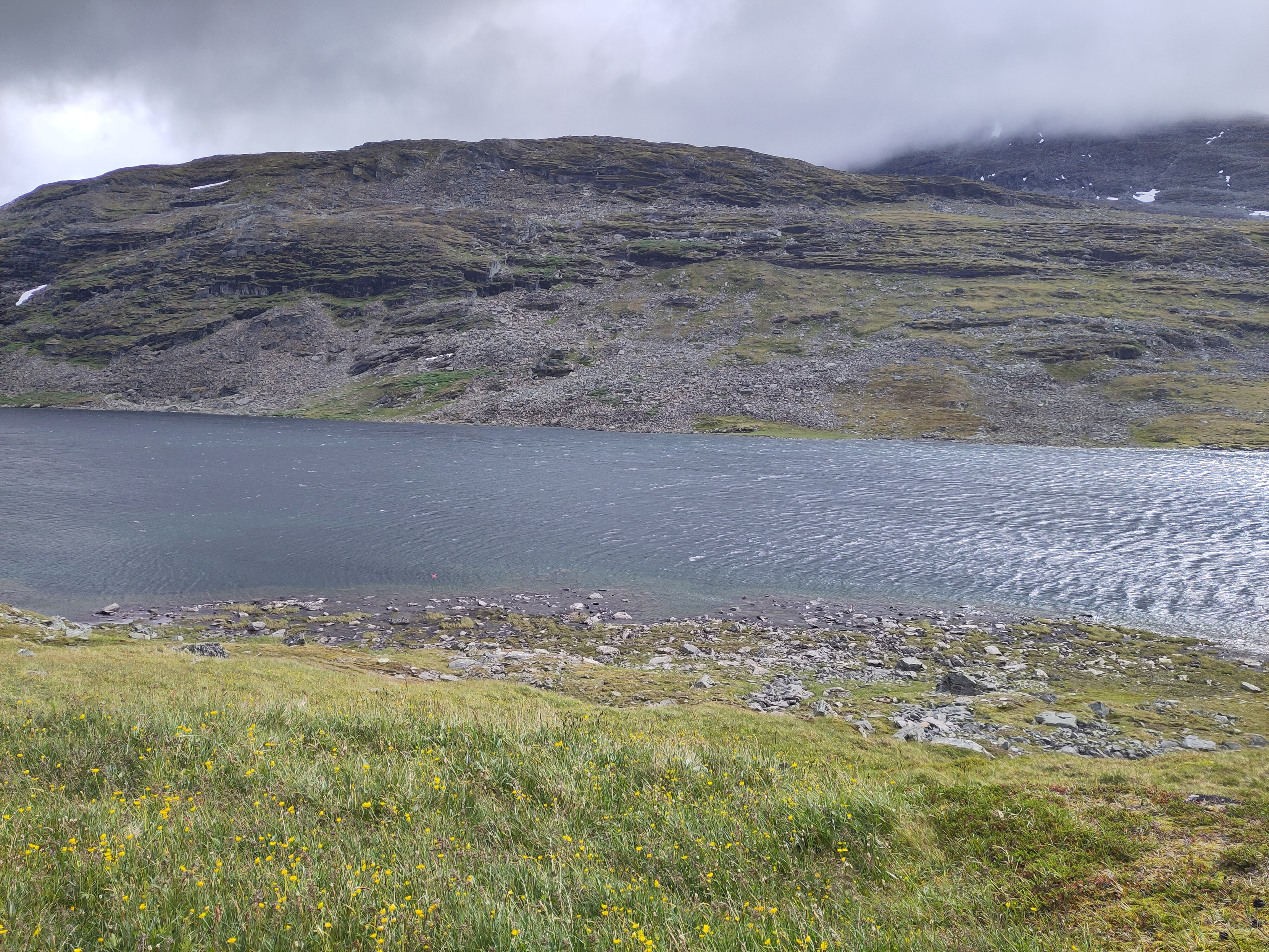 A small lake with clear wave patterns from hard winds at the bottom of a valley.

The foreground is green, but on the other side it is mostly rocks.