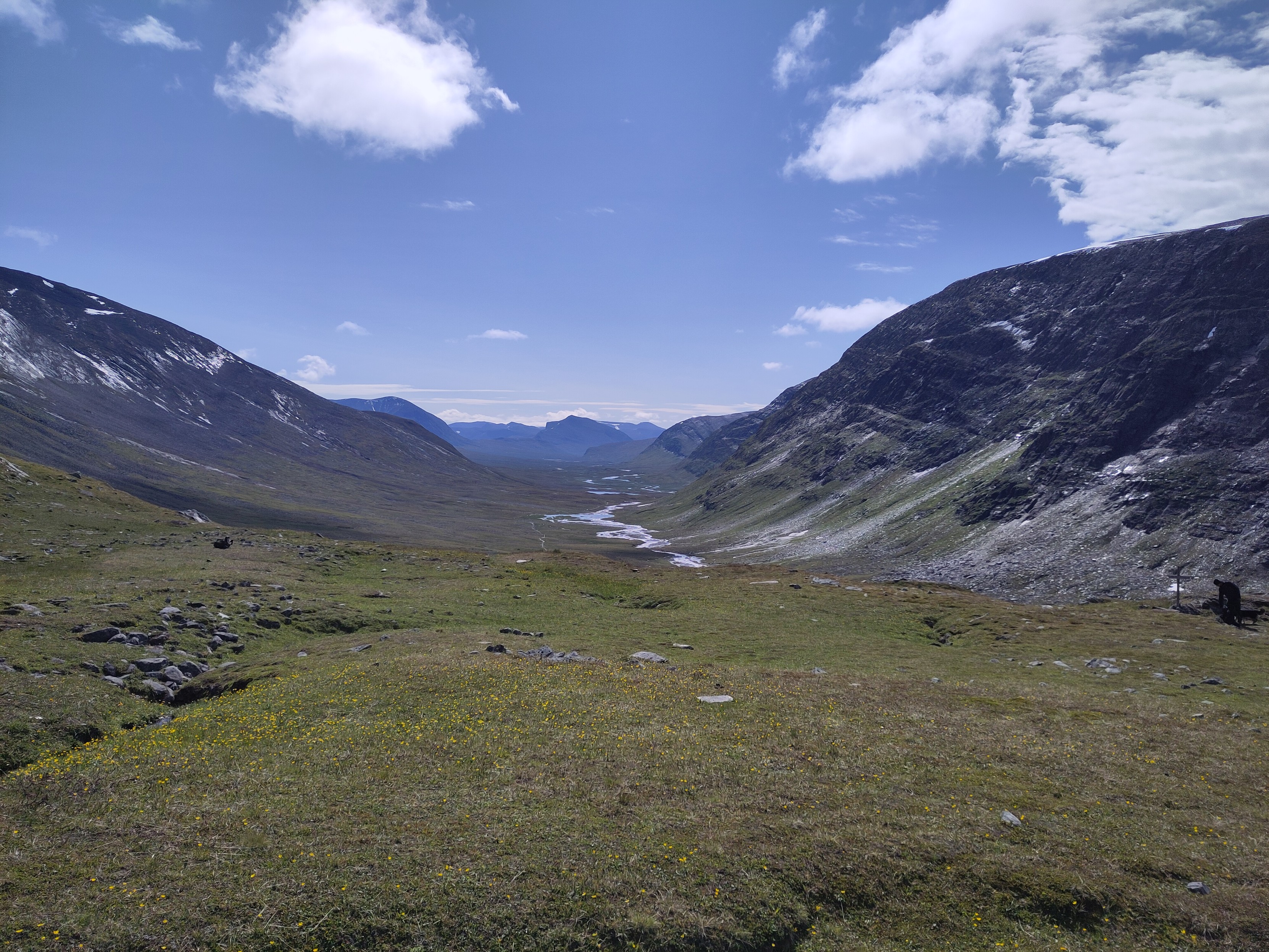 The long wide valley of Čeakčavággi under a blue sky with a few tufty clouds. It goes on until the mountains turn blue from distance.